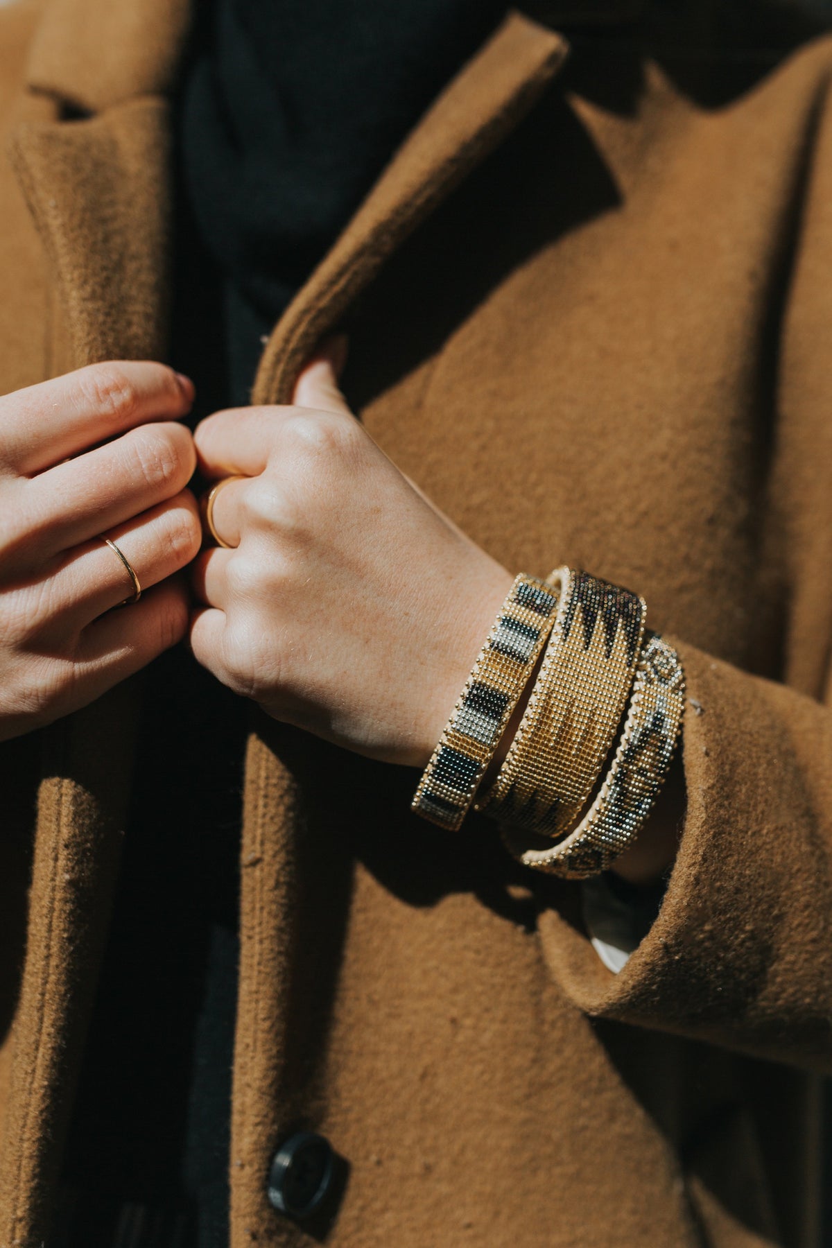 Stacked hand-beaded cuffs worn over a camel wool coat